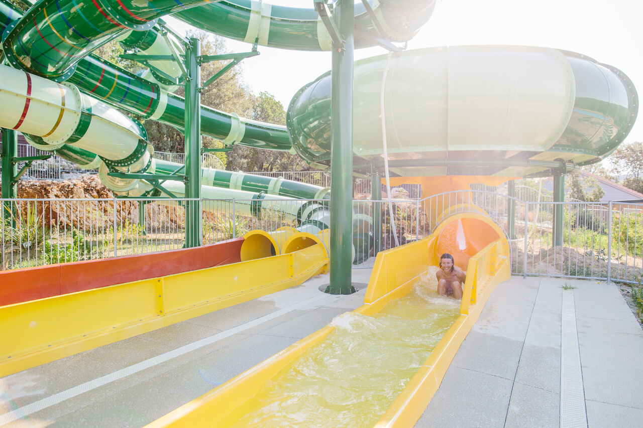 Giant green and yellow water slides, person having fun at LIBRANOO Naturiste Sabliere campsite in Barjac (30).