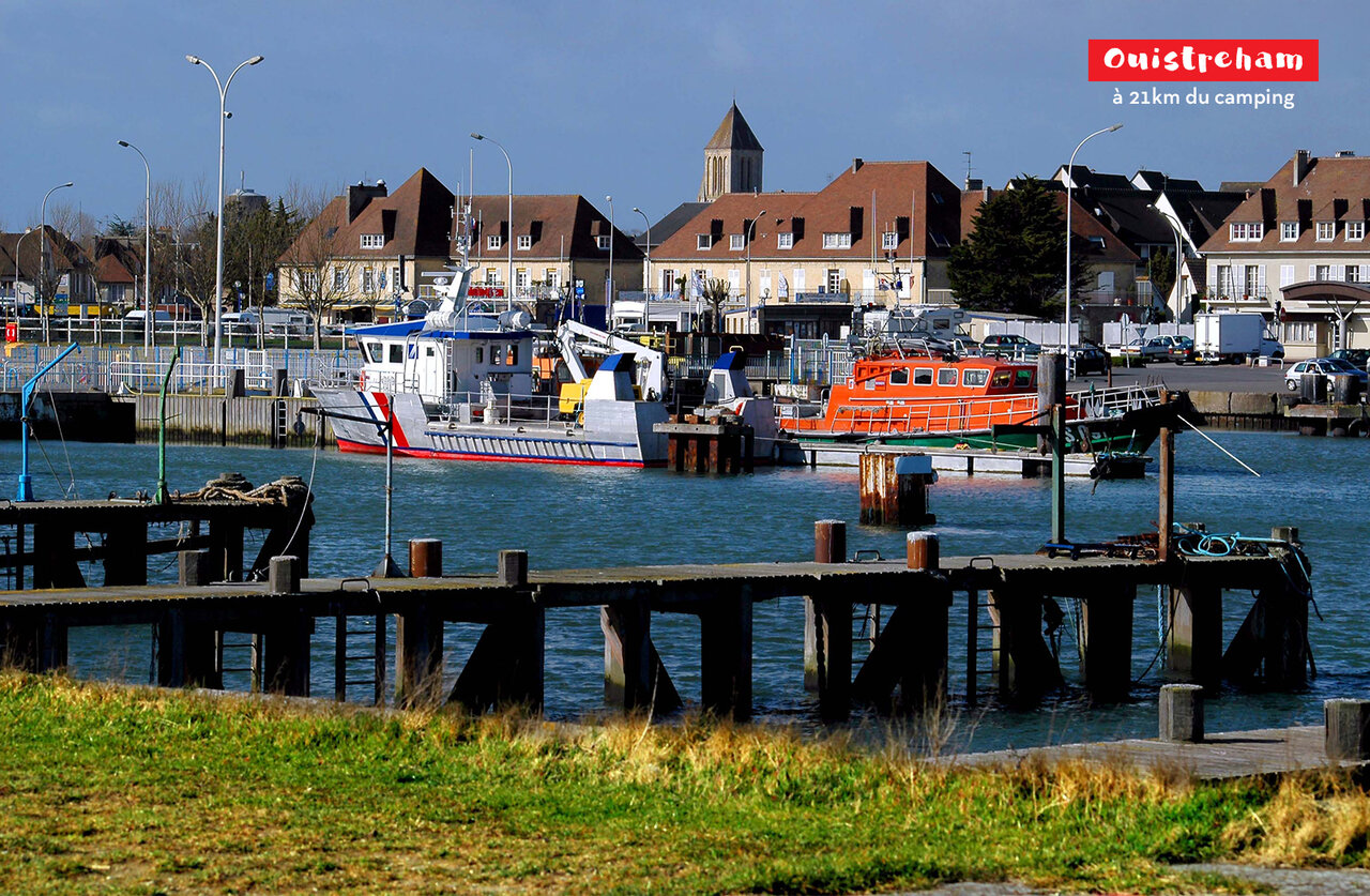 Ouistreham harbor with boats, houses, and church tower in Normandy.