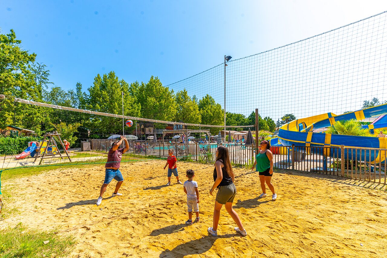 Family playing beach volleyball on sand court, water slides at CAPFUN Duravel.