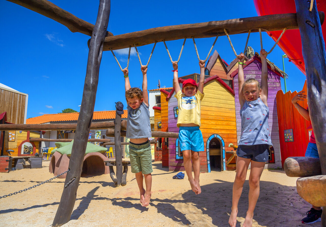 Three smiling children play on monkey bars at CAPFUN Ecureuils campsite in JARD SUR MER (85).