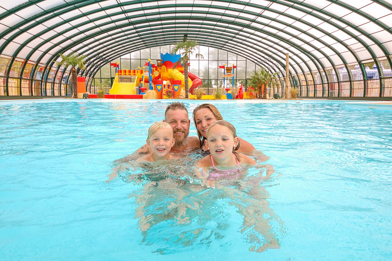 Smiling family in covered swimming pool with water games at CAPFUN Eibernest.