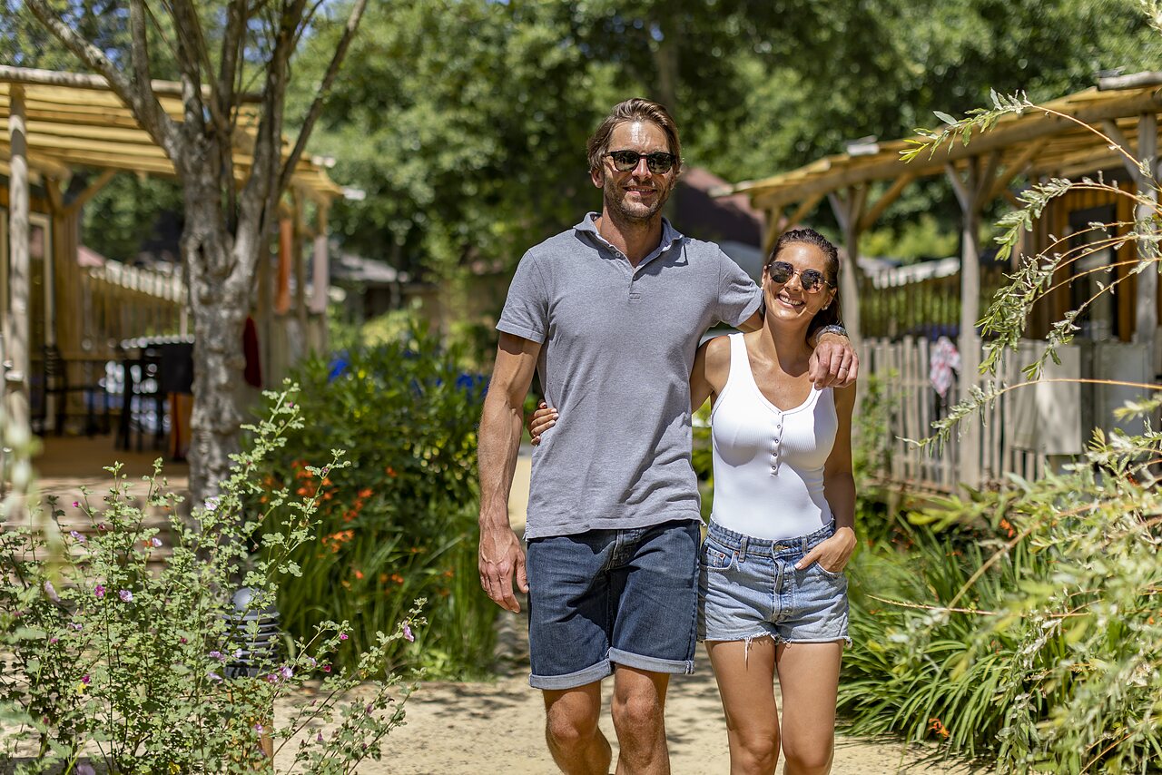 Smiling couple walking green path, nature at CAPFUN El Moli campsite in Elne (66).