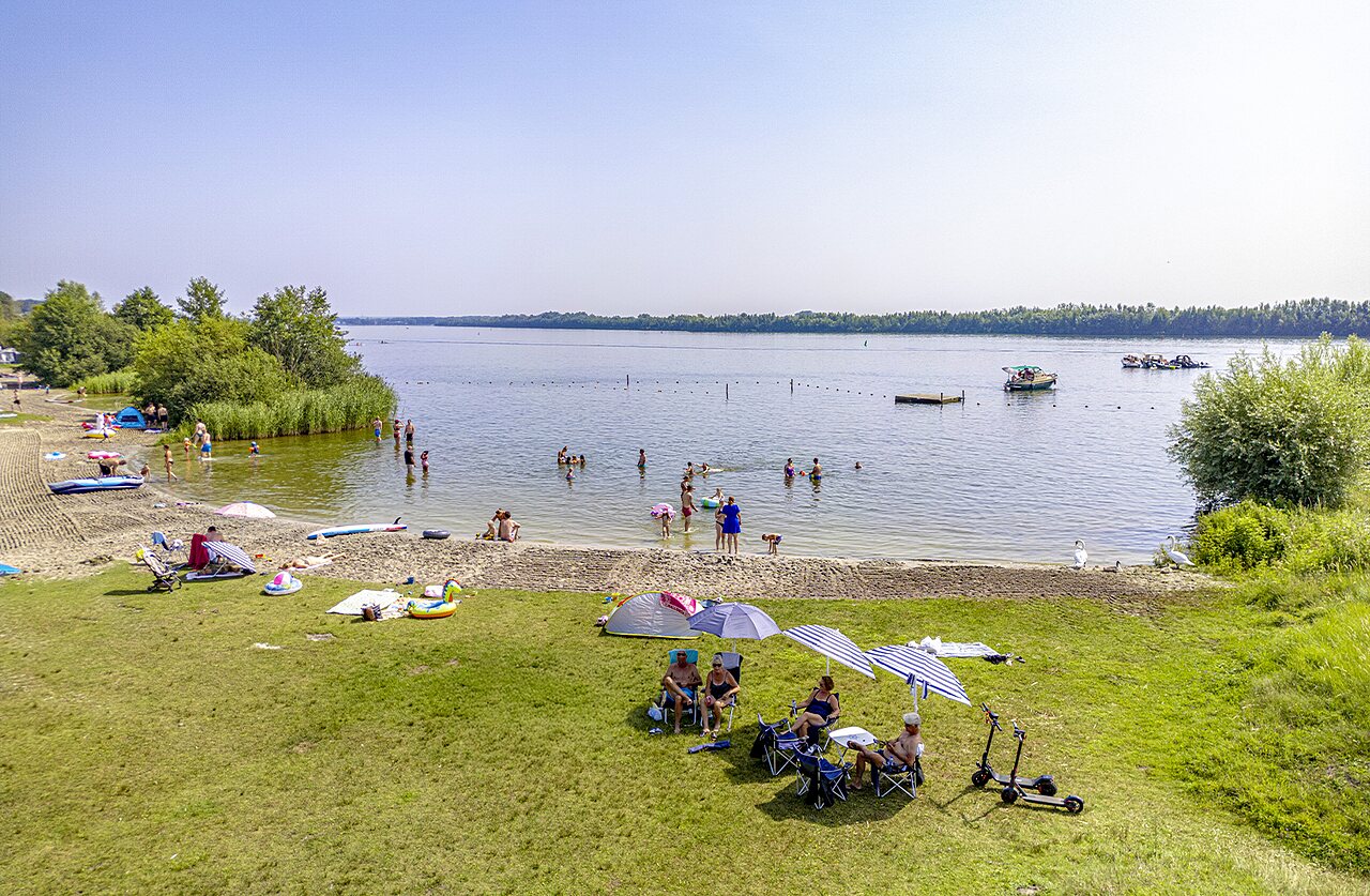 Sandy beach with swimmers and water activities at CAPFUN Erkemederstrand campsite in Zeewolde.