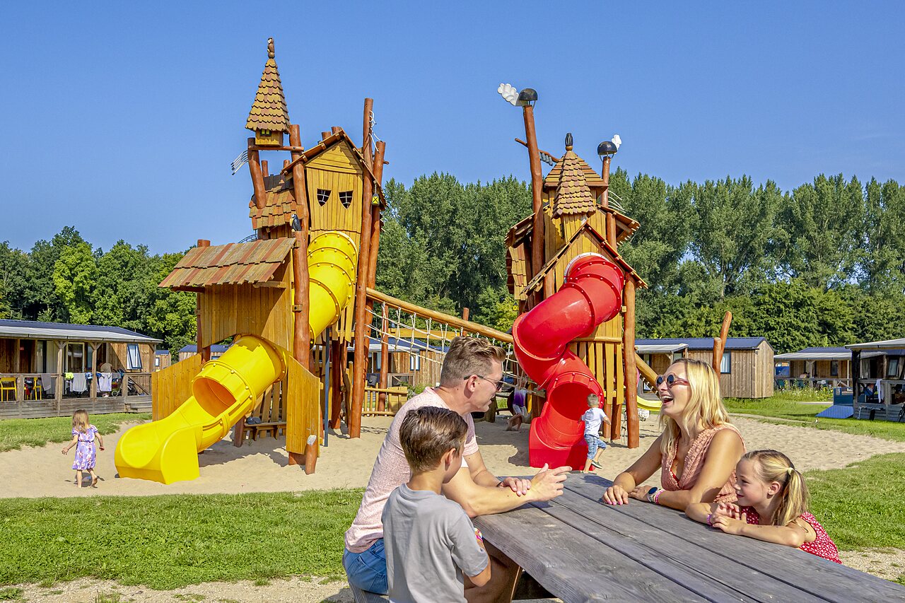 Playground with slides and happy family at CAPFUN Erkemederstrand campsite in Zeewolde.