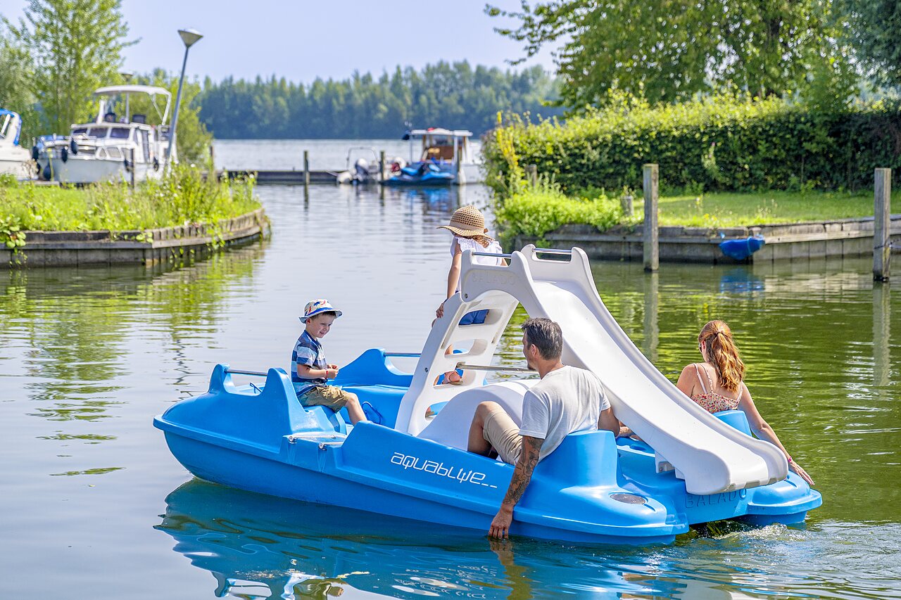 Family on pedal boat with water slide at CAPFUN Erkemederstrand campsite in Zeewolde.