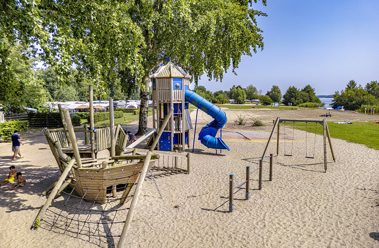 Playground with slide, swings, and sandy beach at CAPFUN Erkemederstrand campsite in Zeewolde.