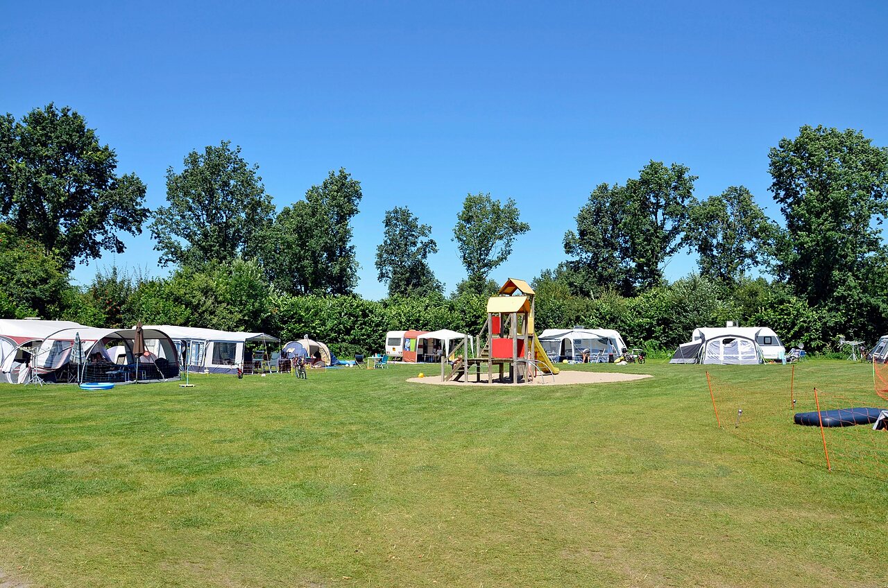Green camping pitches with playground and caravans at CAPFUN Erkemederstrand campsite in Zeewolde.