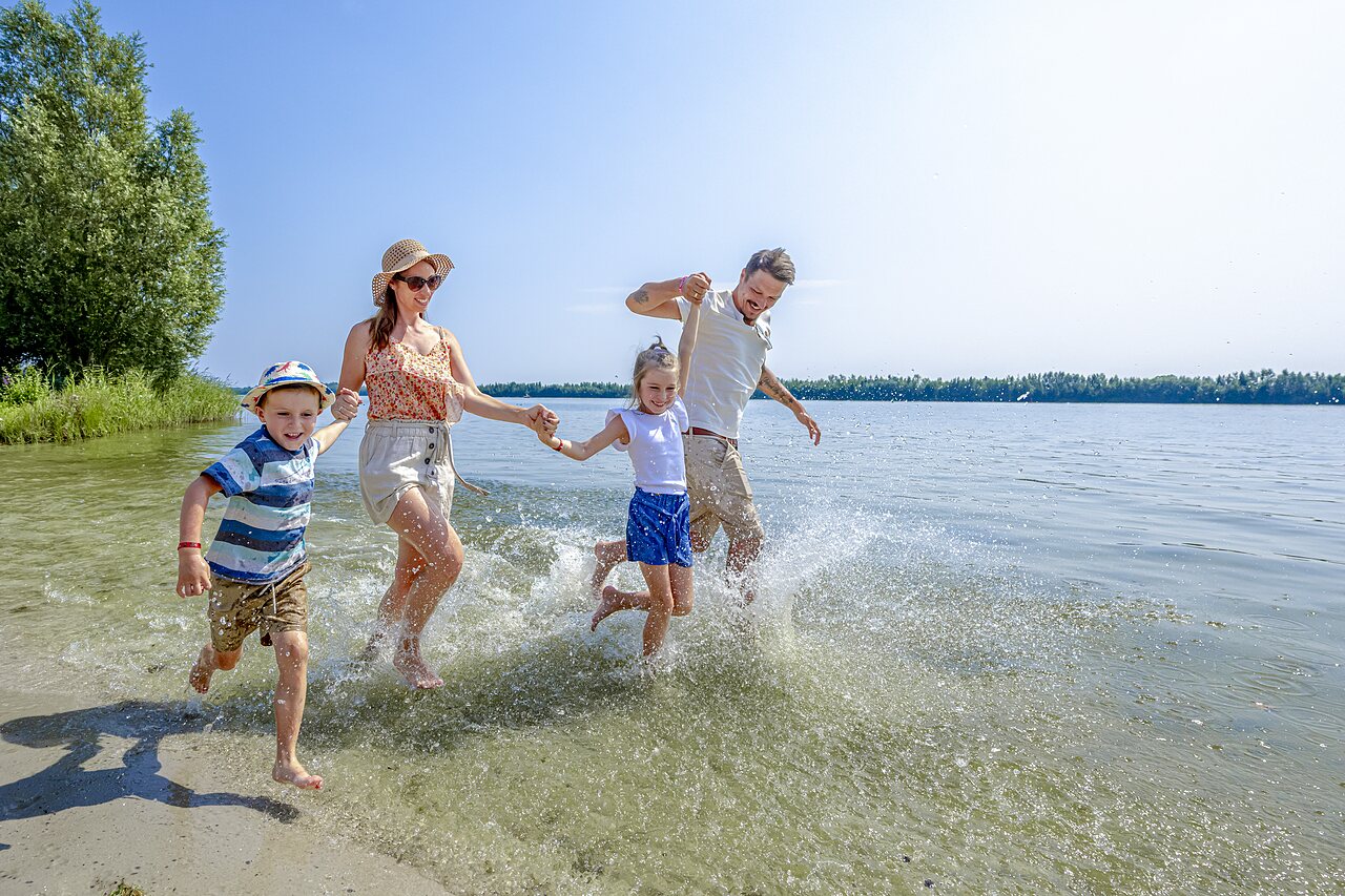 Happy family running and splashing in shallow water at CAPFUN Erkemederstrand campsite in Zeewolde.