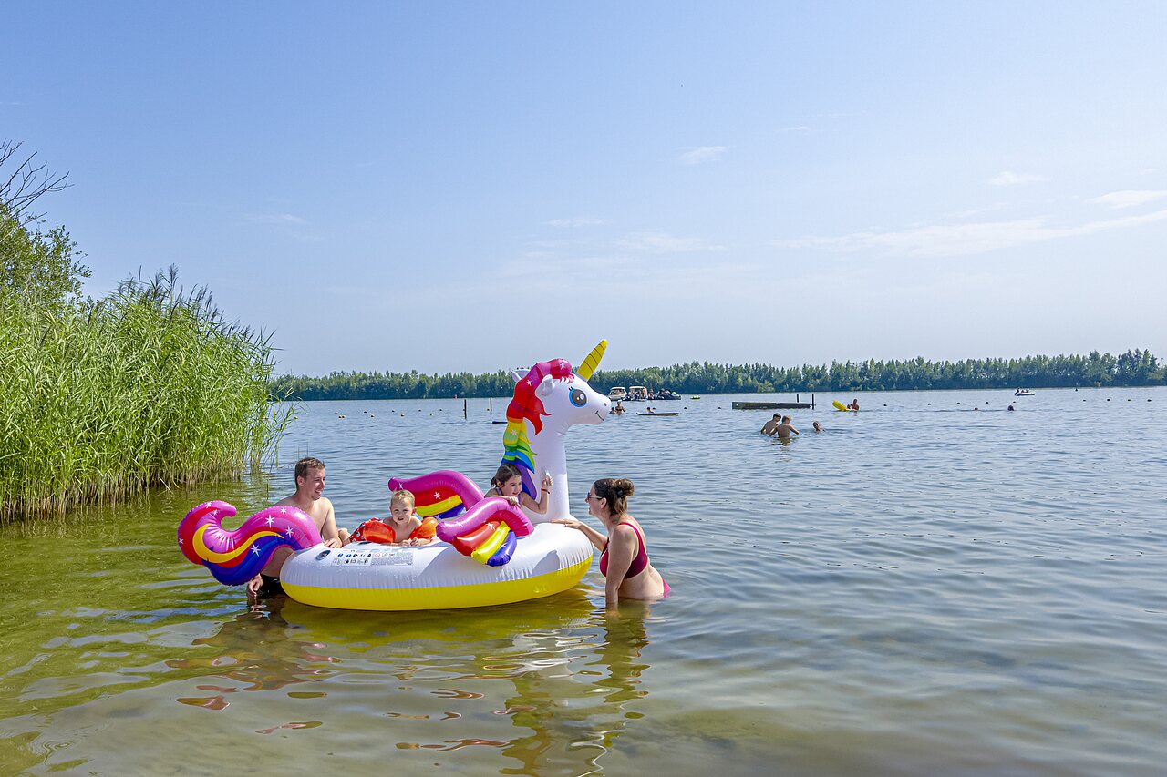 Family playing in lake with inflatable unicorn at CAPFUN Erkemederstrand in Zeewolde.
