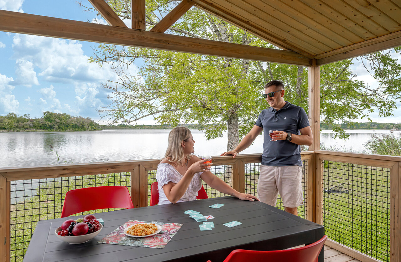 Accommodation terrace, couple and lake view at CLICOCHIC Etang de la Mutche campsite in HARPRICH (57).