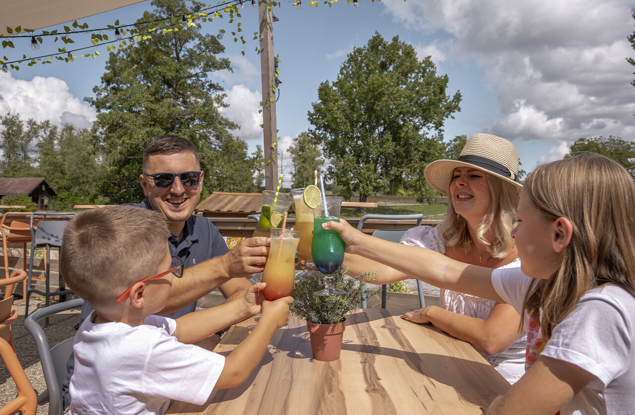 Family toasting cocktails on bar terrace at CLICOCHIC campsite in HARPRICH.