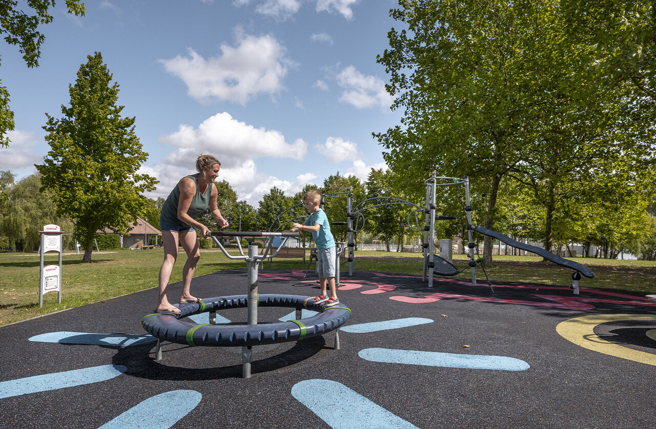 Mother and child on rotating playground equipment at camping CLICOCHIC Etang de la Mutche in HARPRICH.
