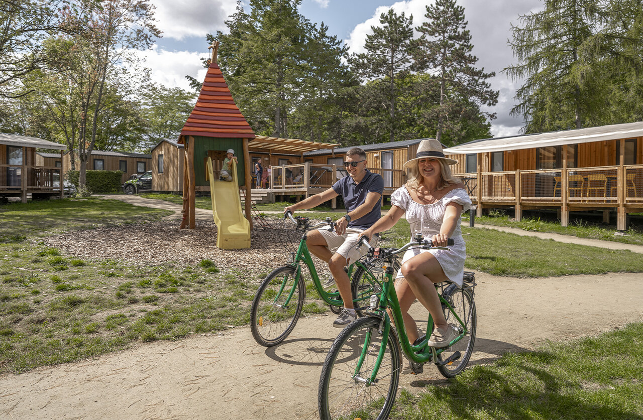 Couple cycling, child on slide, accommodation at CLICOCHIC Etang de la Mutche HARPRICH (57).