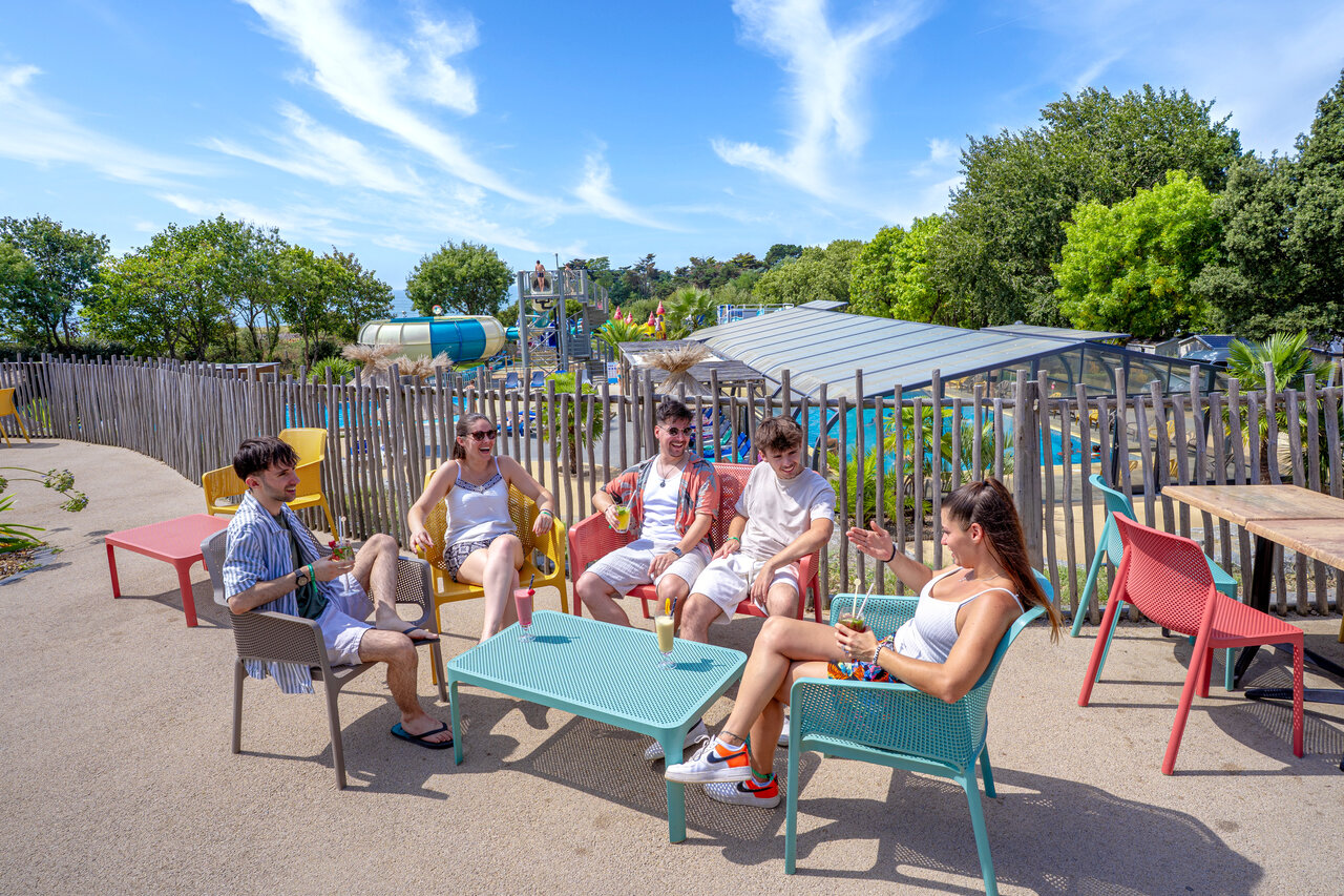 Group of friends at outdoor bar with water slides and pool at CAPFUN L'Eve campsite in Saint-Marc-sur-Mer (44).
