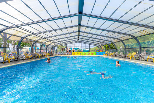Heated indoor swimming pool with swimmers and chairs at CAPFUN L'Eve campsite in Saint-Marc-sur-Mer (44).