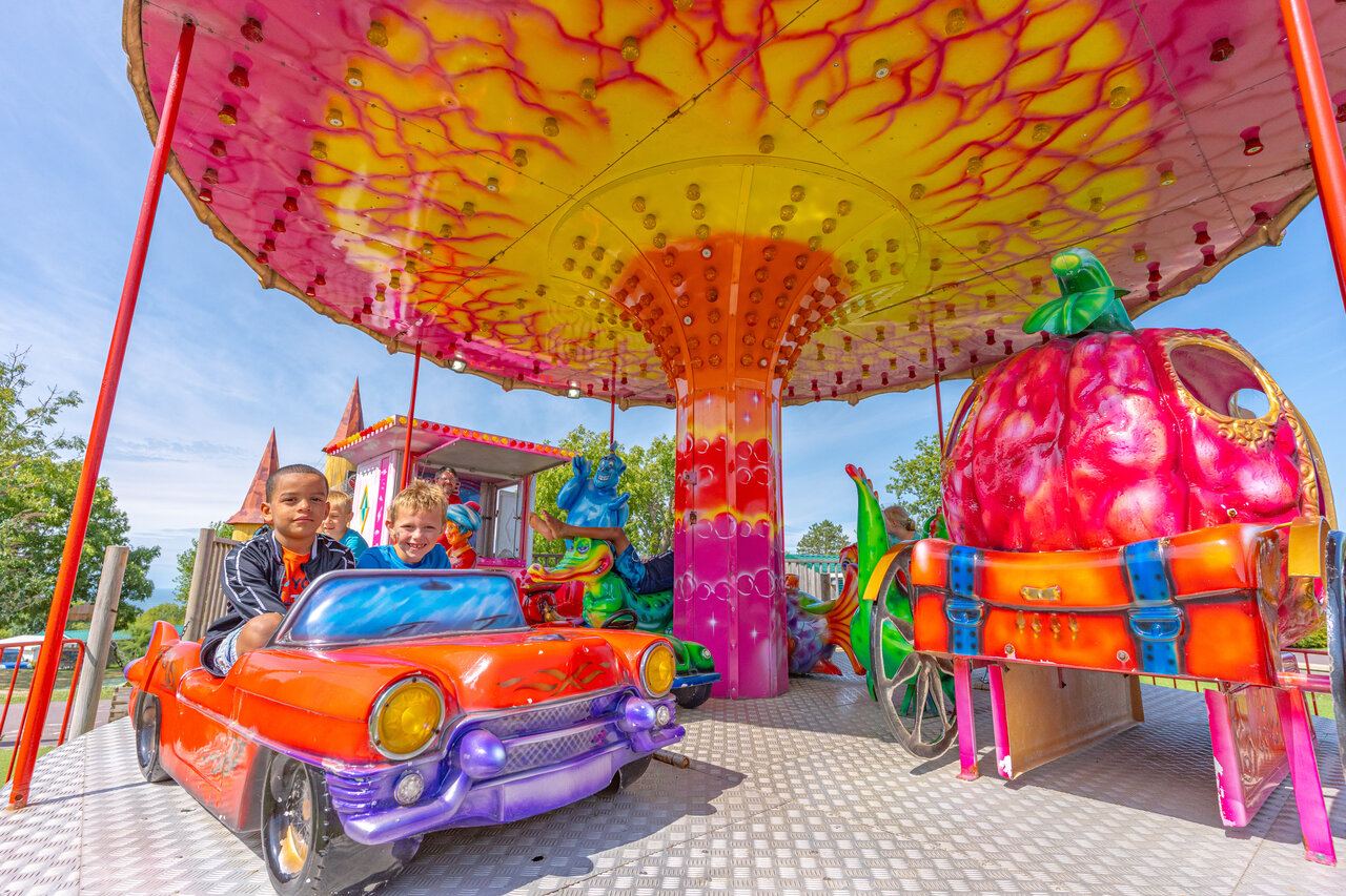 Smiling children on colorful carousel car ride at CAPFUN Falaises campsite.