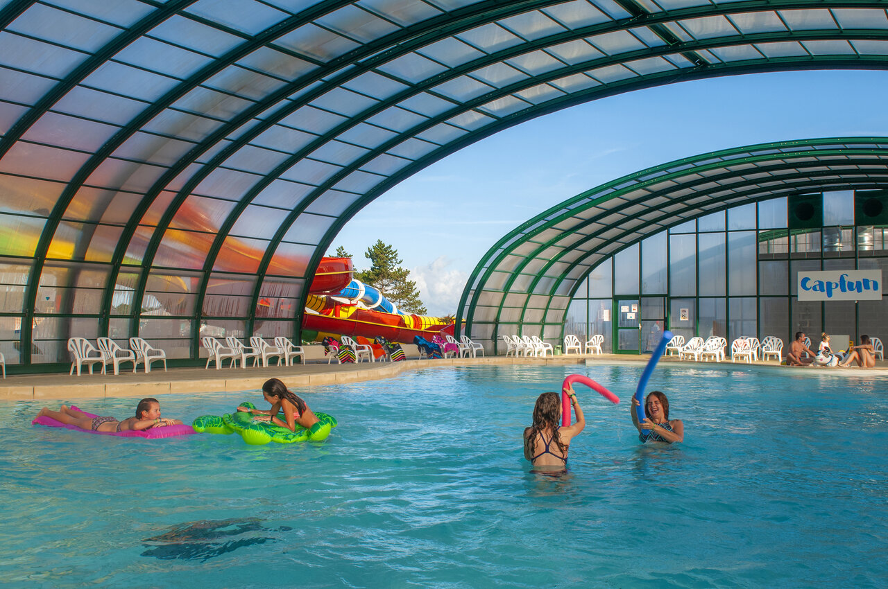 Covered swimming pool with slides and children playing at CAPFUN Falaises campsite in Gonneville sur Mer.