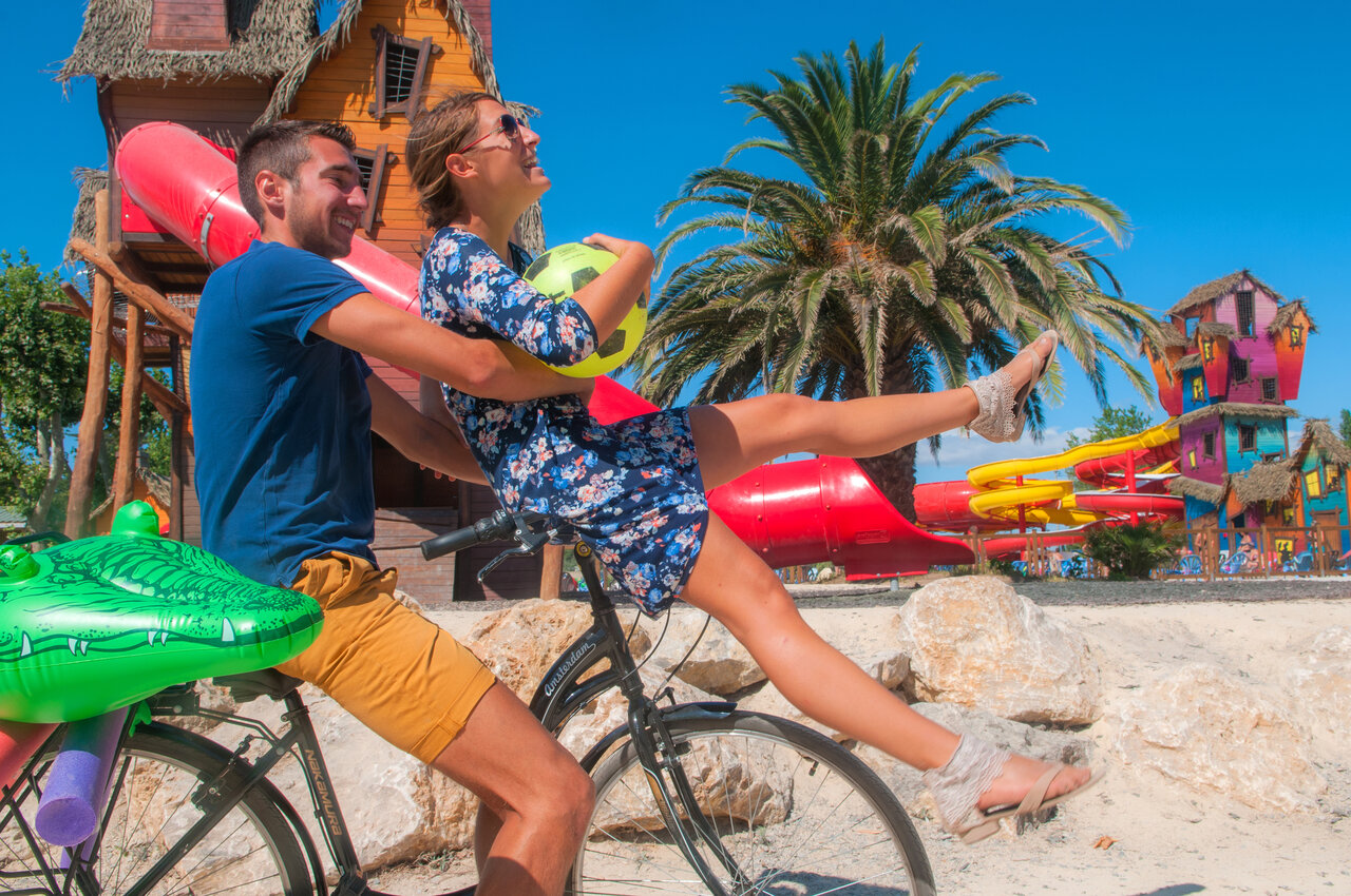 Happy couple on bike in front of colorful water slides at CAPFUN F�erix campsite in MARSEILLAN PLAGE (34)