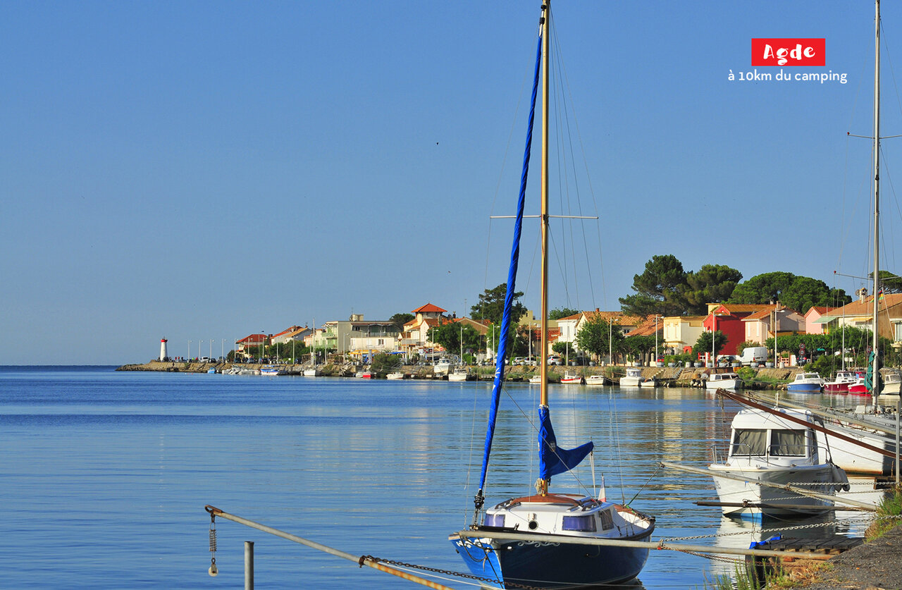 Port of Agde with sailboats, colorful houses and lighthouse, near Marseillan Plage.