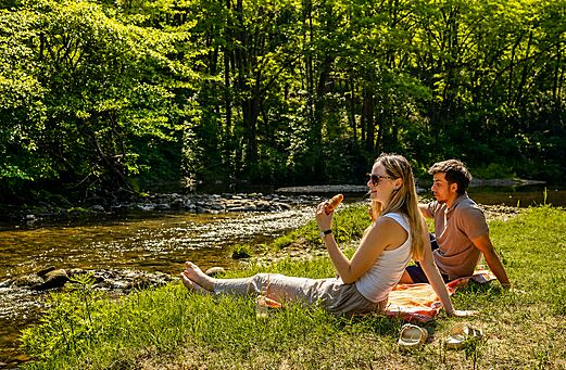 Couple picnicking by the river, green surroundings at camping CLICOCHIC Filament in Thoiras.