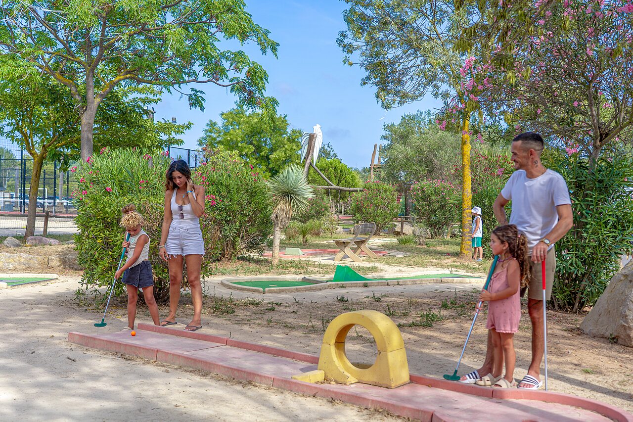 Family playing mini-golf on an outdoor course at CAPFUN Fleurs d'Agde campsite in AGDE (34).