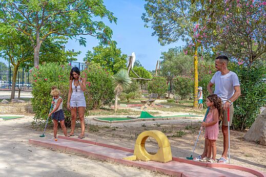 Family playing mini-golf on an outdoor course at CAPFUN Fleurs d'Agde campsite in AGDE (34).