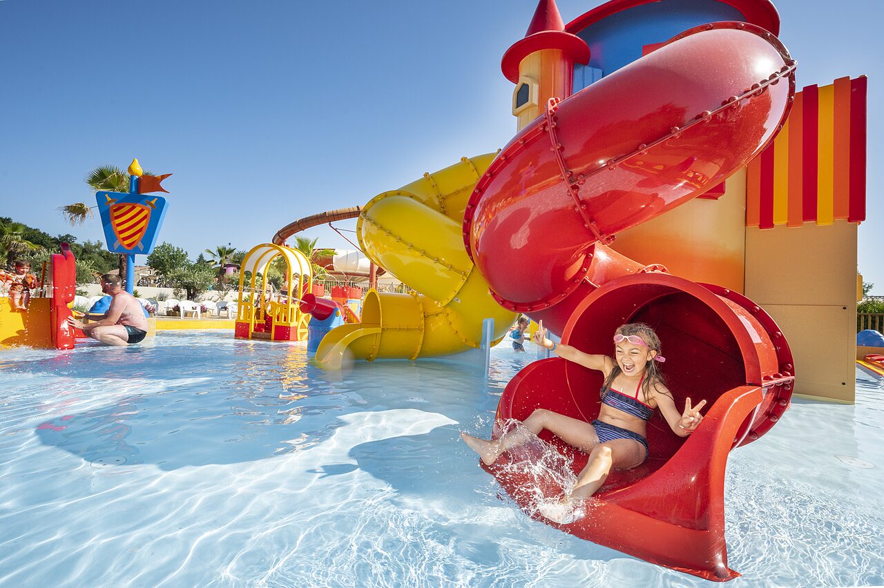 Smiling girl sliding down red water slide in pool at CAPFUN Forges campsite in Avrille (85).