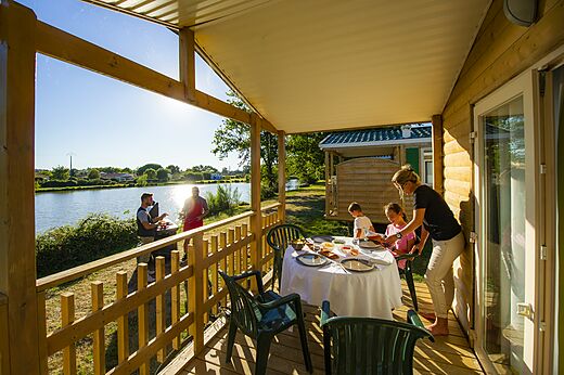 Family dining on Mobil-home terrace by lake at CAPFUN Forges campsite in Avrille (85).