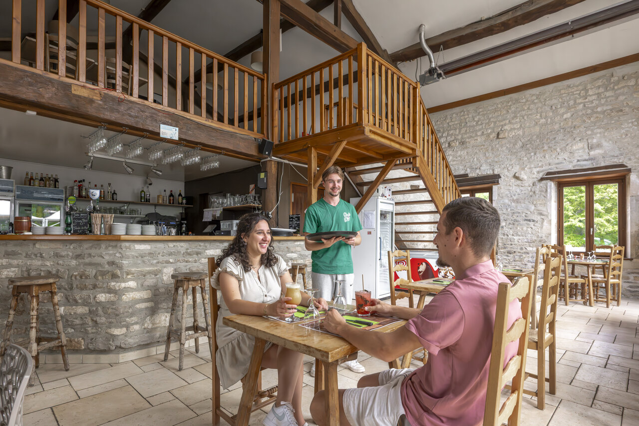 Restaurant-bar interior, couple and server at CLICOCHIC Forge Sainte Marie campsite Thonnance-les-Moulins.
