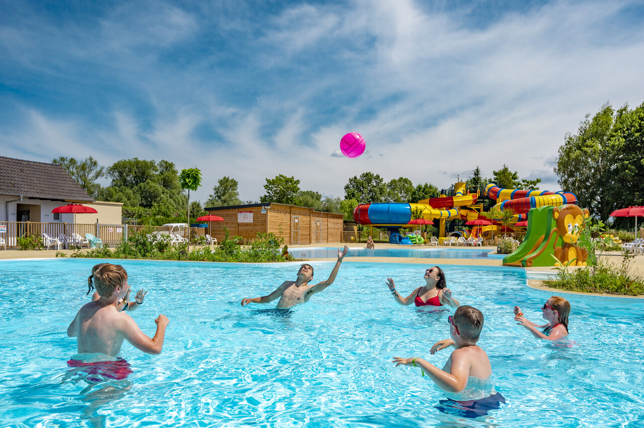 Family playing ball in swimming pool with waterslides at CAPFUN Fort Falabraque campsite in Seltz (67).