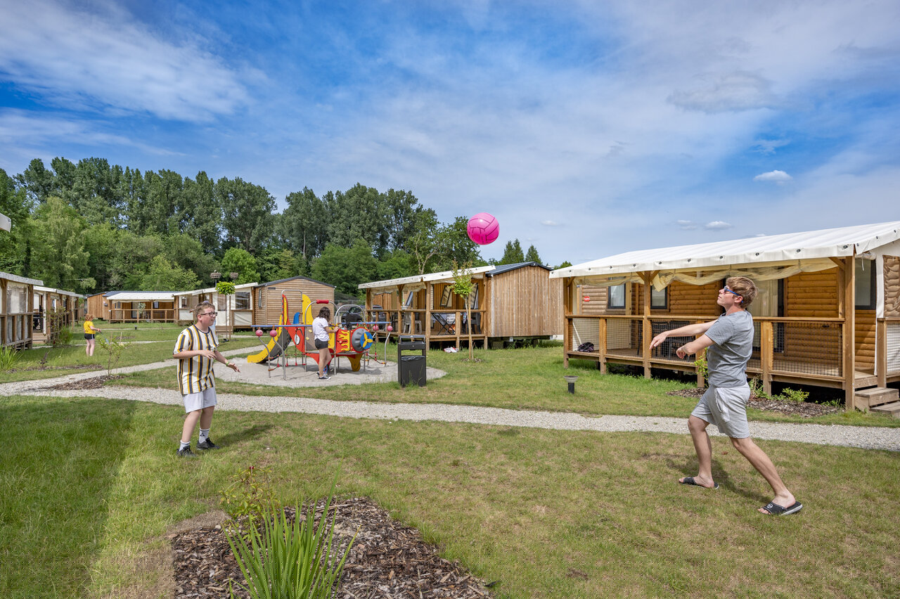 Young people playing volleyball near playground and mobile homes at CAPFUN Fort Falabraque campsite in Seltz (67).