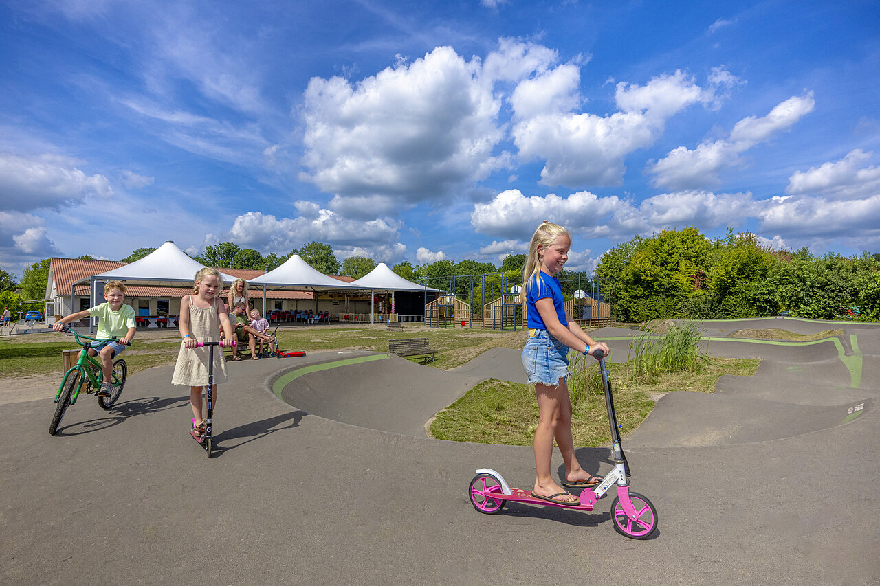 Children on pump track with scooters and bikes, CAPFUN De Fruithof campsite.