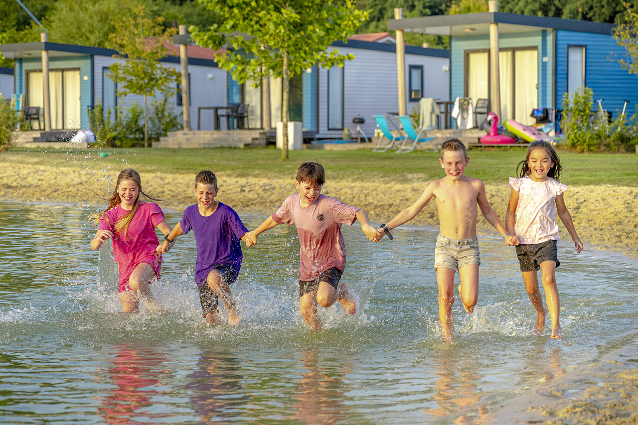 Happy children running in shallow water in front of mobile homes at CAPFUN De Fruithof campsite in Klijndijk.