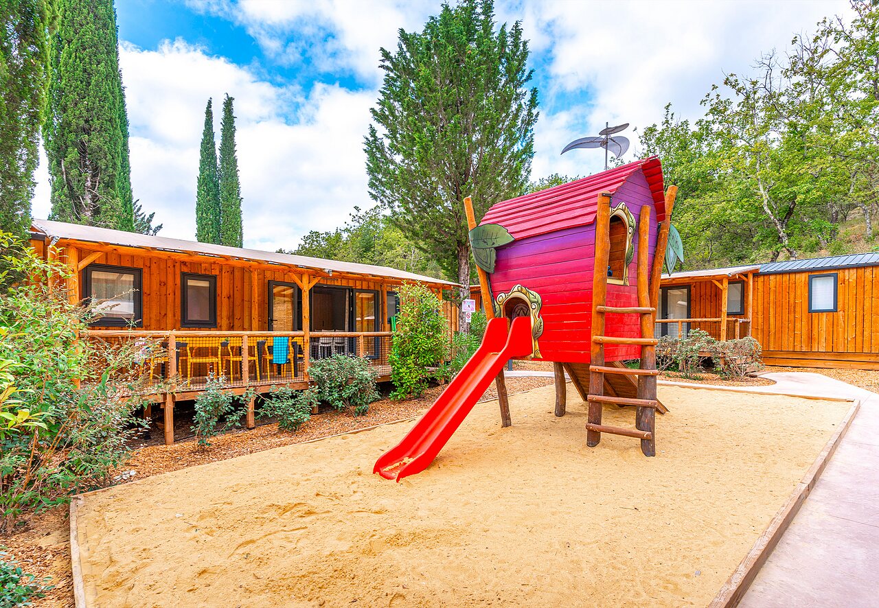 Playground with slide and wooden accommodations at CAPFUN Fumades campsite (30).