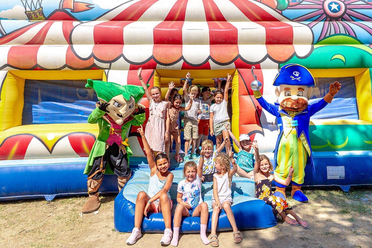 Children and mascots in front of bouncy castle at CAPFUN Fumades campsite in ALLEGRE-LES-FUMADES.