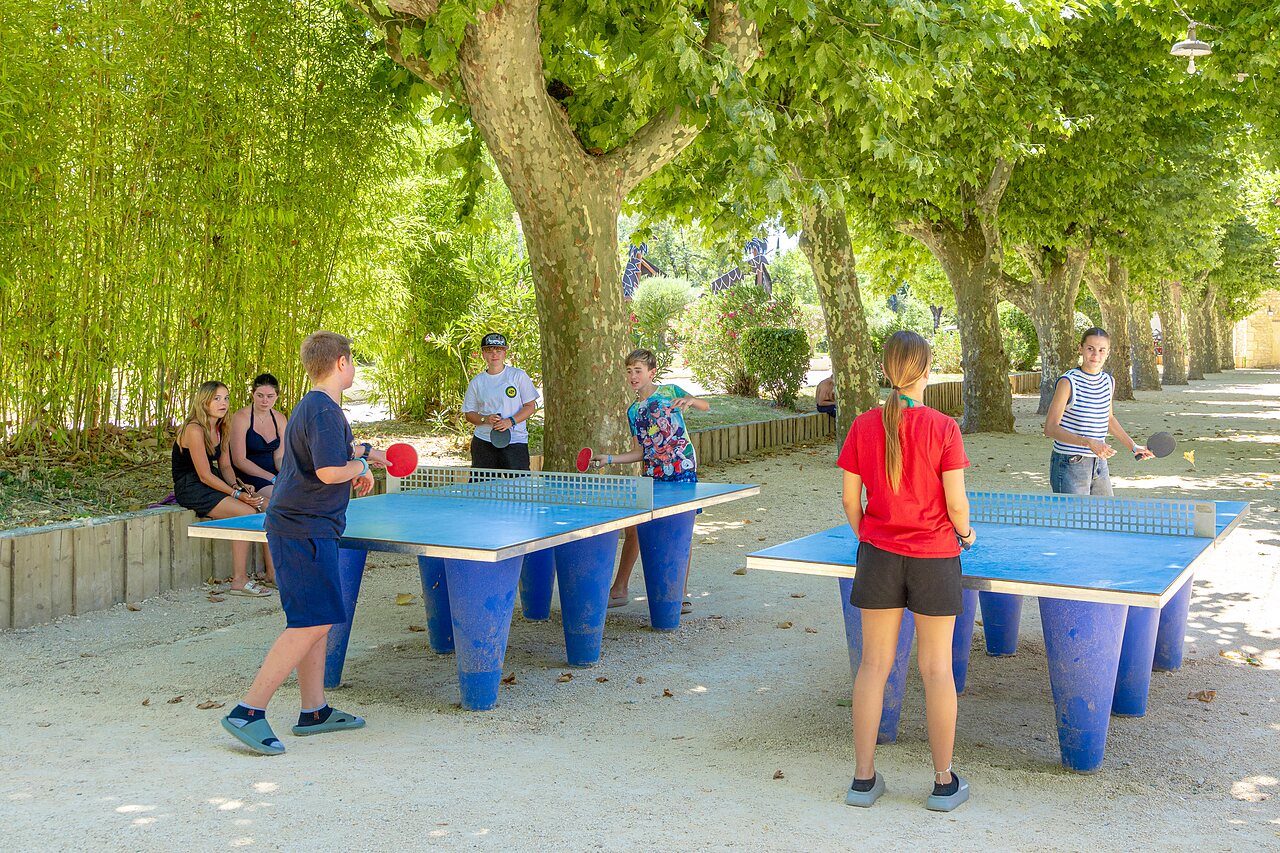 Young people playing outdoor shaded table tennis at CAPFUN Fumades campsite.