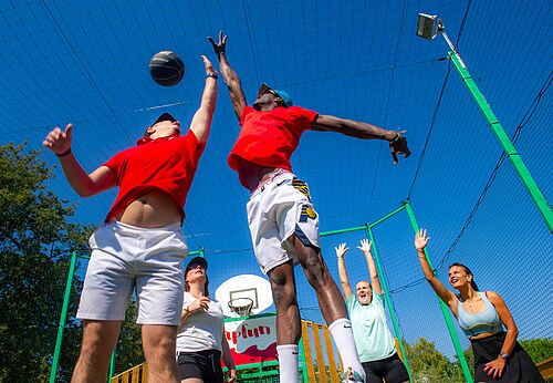 Basketball players in game on multisport court at CAPFUN Fumades campsite.