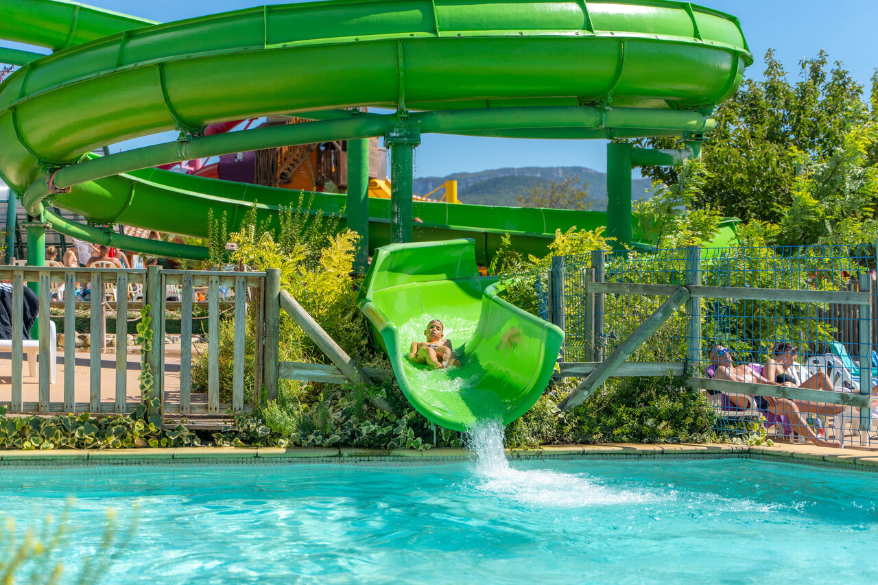 Child on giant green water slide and pool at CAPFUN Grand Lierne campsite in CHATEAUDOUBLE (26).