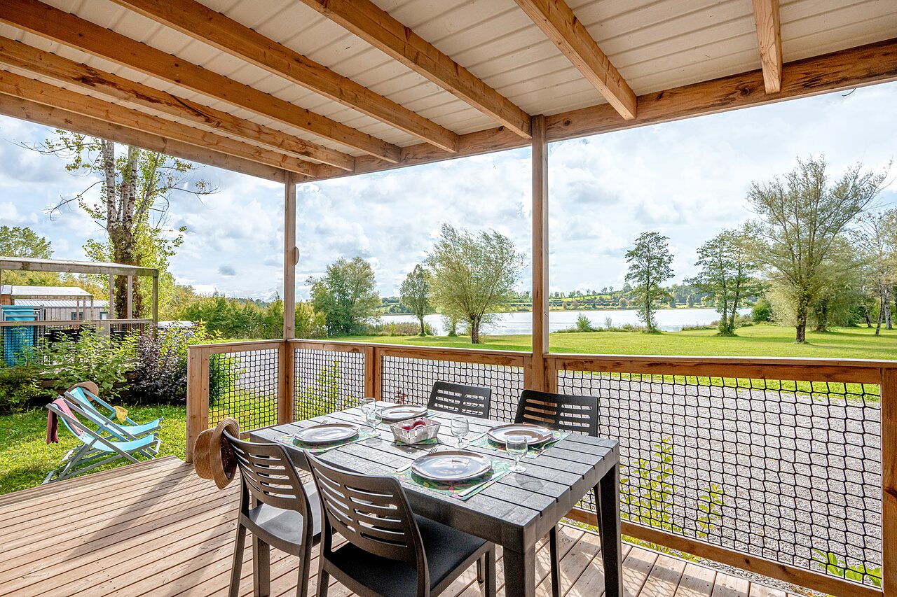 Covered accommodation terrace, set table, lake view at camping CLICOCHIC Grisi�re in Clairvaux-les-Lacs.