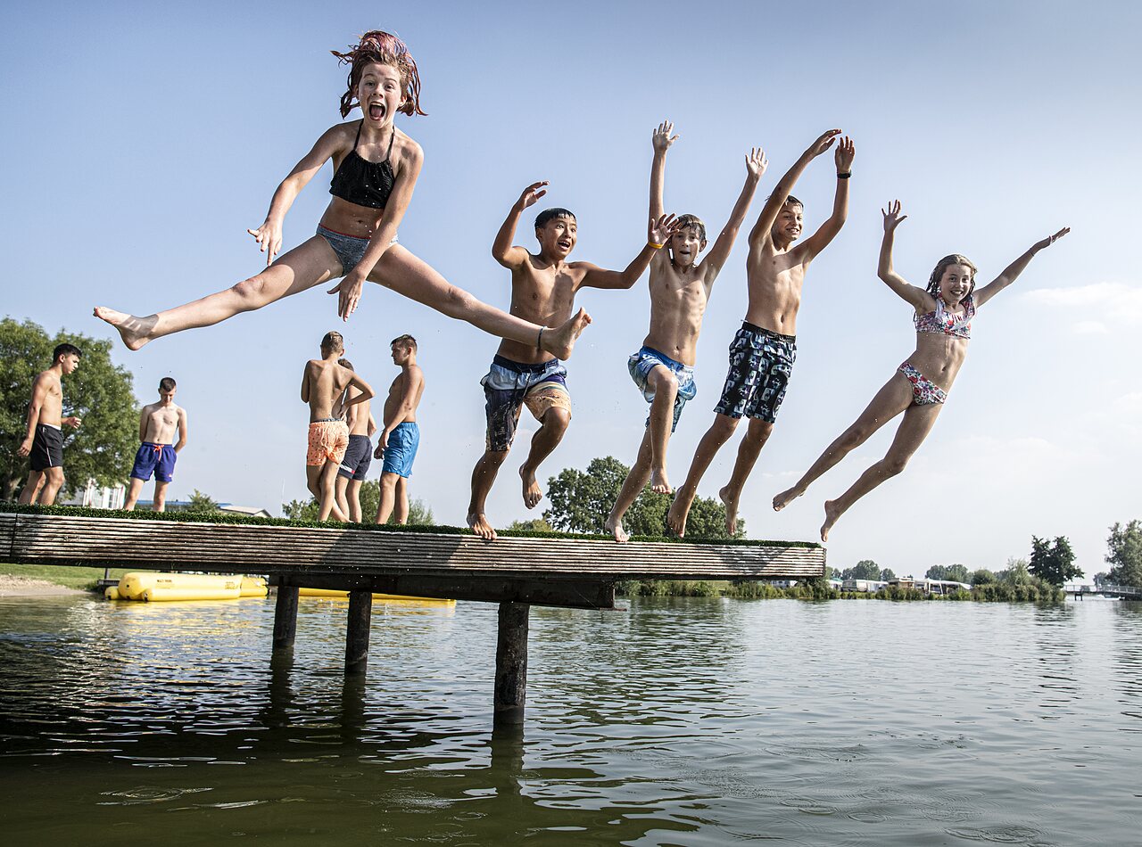 Children happily jumping from a pontoon into the lake at CAPFUN Groene Eiland campsite in Appeltern.