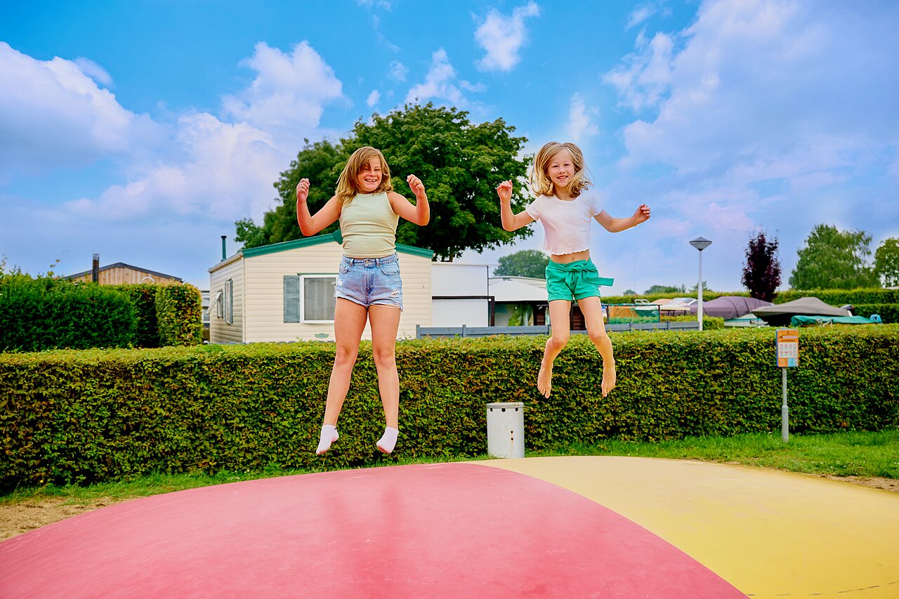 Two girls happily jumping on an inflatable bouncy pillow at CAPFUN Groene Eiland campsite in Appeltern.