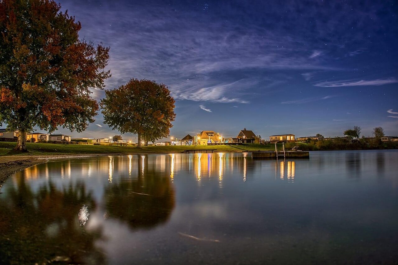 Illuminated lake at night and accommodations at CAPFUN Groene Eiland campsite in Appeltern.