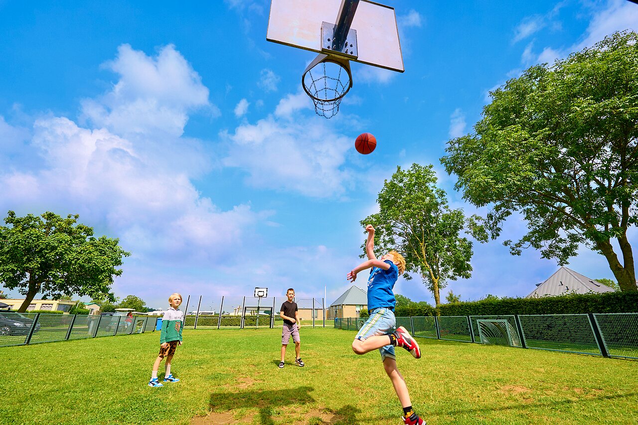 Children playing basketball on multi-sport court at CAPFUN Groene Eiland campsite in Appeltern.