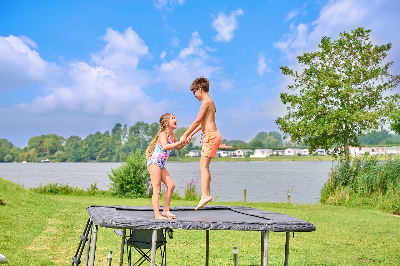 Two children jumping on outdoor trampoline by the lake at CAPFUN Groene Eiland campsite in Appeltern.