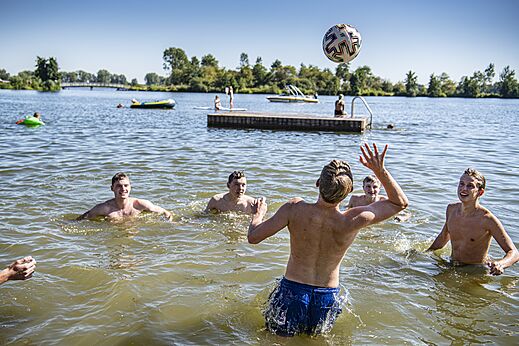 Young people playing volleyball in lake water at CAPFUN Groene Eiland campsite in Appeltern.