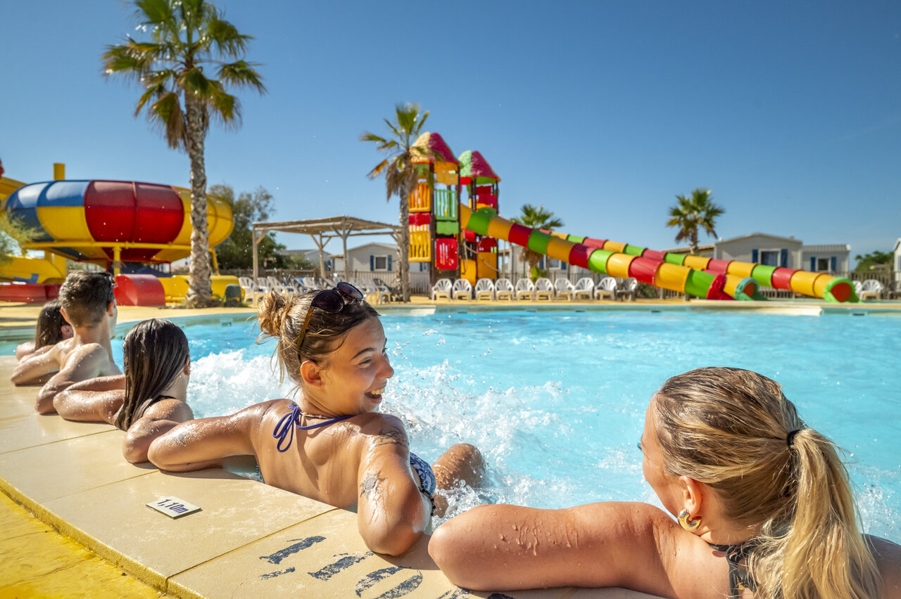 Outdoor swimming pool with colorful water slides and bathers at VAGUES OCEANES Hamacs campsite in Fleury (11).