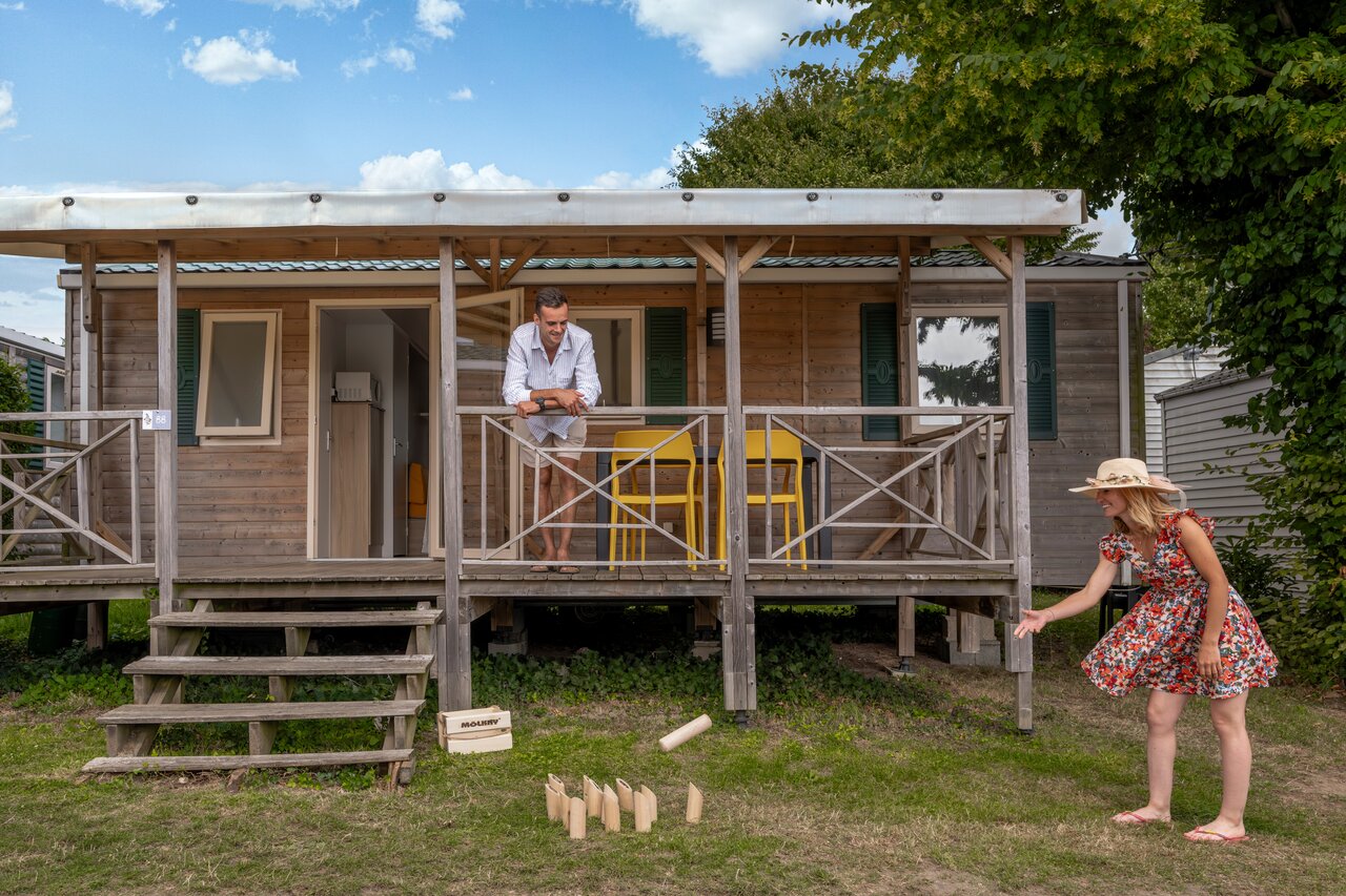 Wooden mobile home with terrace, couple playing M�lkky at CLICOCHIC Haras de Deauville campsite in Touques.