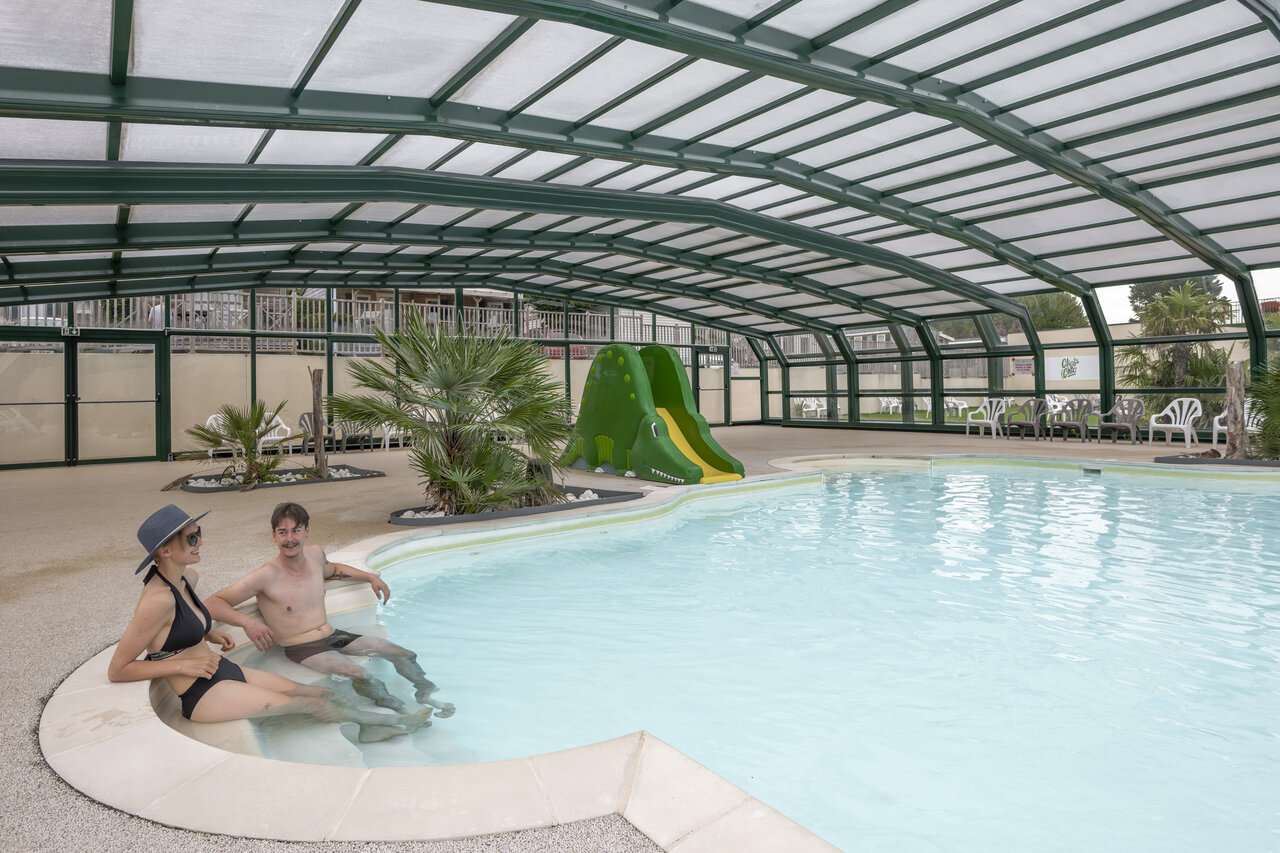 Covered swimming pool with crocodile slide and couple at CLICOCHIC Haras de Deauville campsite in Touques (14).