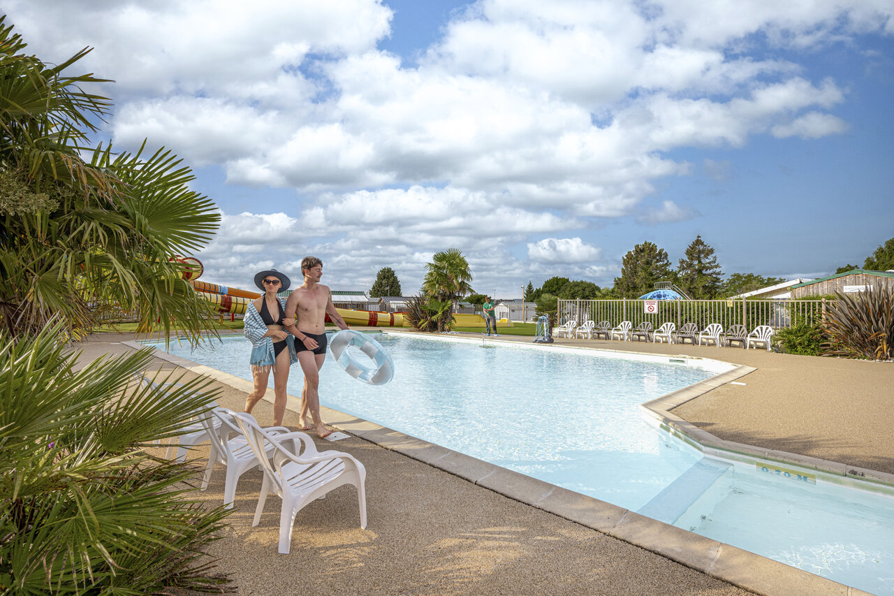 Couple at outdoor pool with slides at CLICOCHIC Haras de Deauville campsite.
