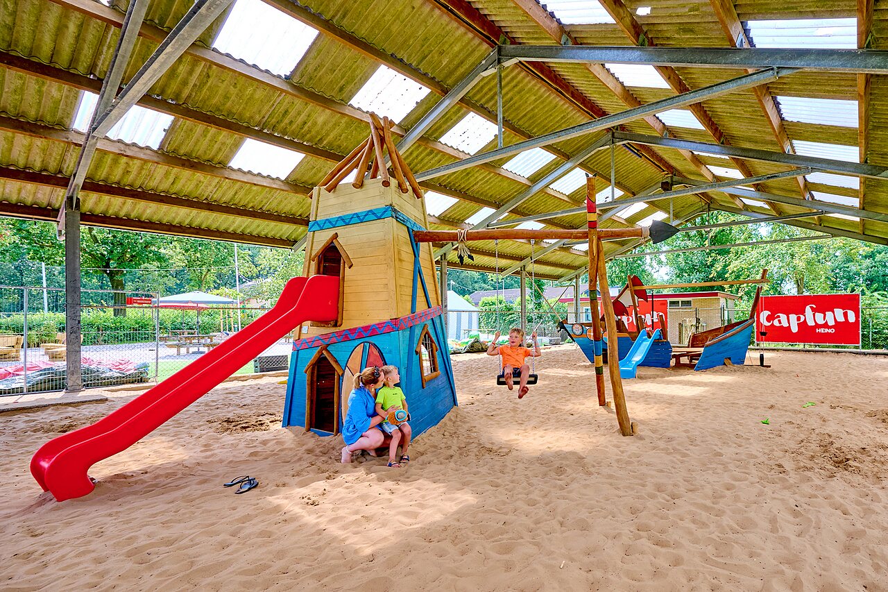 Covered playground with slide, swings and sand at CAPFUN Heino campsite in Heino.